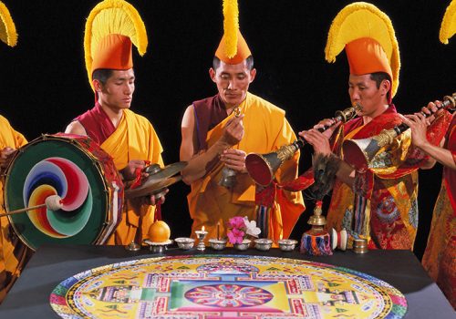 monks with traditional instruments around sand mandala