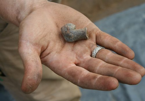 hand holds small piece of clay pipe artifact