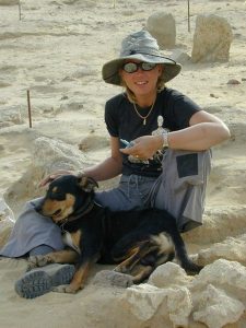 Jessica Kaiser sits in the sand at a dig site with her dog