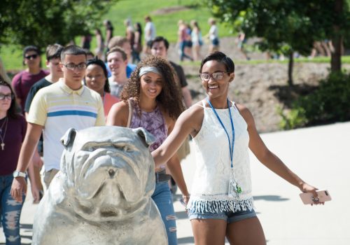 Student patting Rocky the Bulldog statue