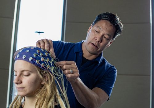 Patrick Foo attaches wires to a 64-channel electroencephalogram (EEG) cap that monitors brain activity