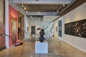 Ceramic sculpture, abstract, but referencing human body form, is on pedestal with other works in the background