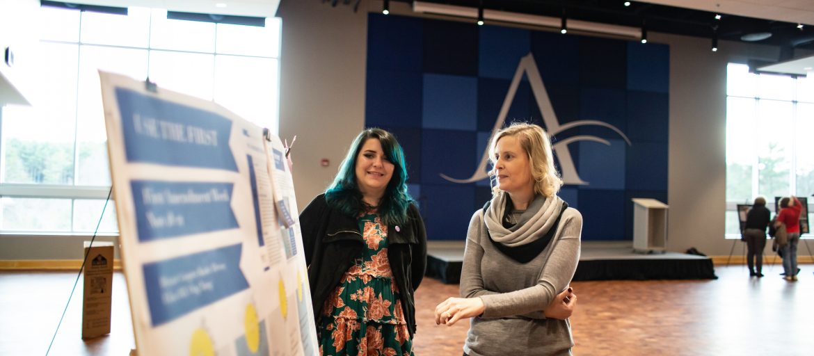 a student and professor look at a poster