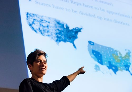Moon Duchin stands in front of maps
