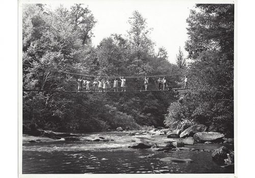 old photo of children standing on a rope bridge above a mountain stream