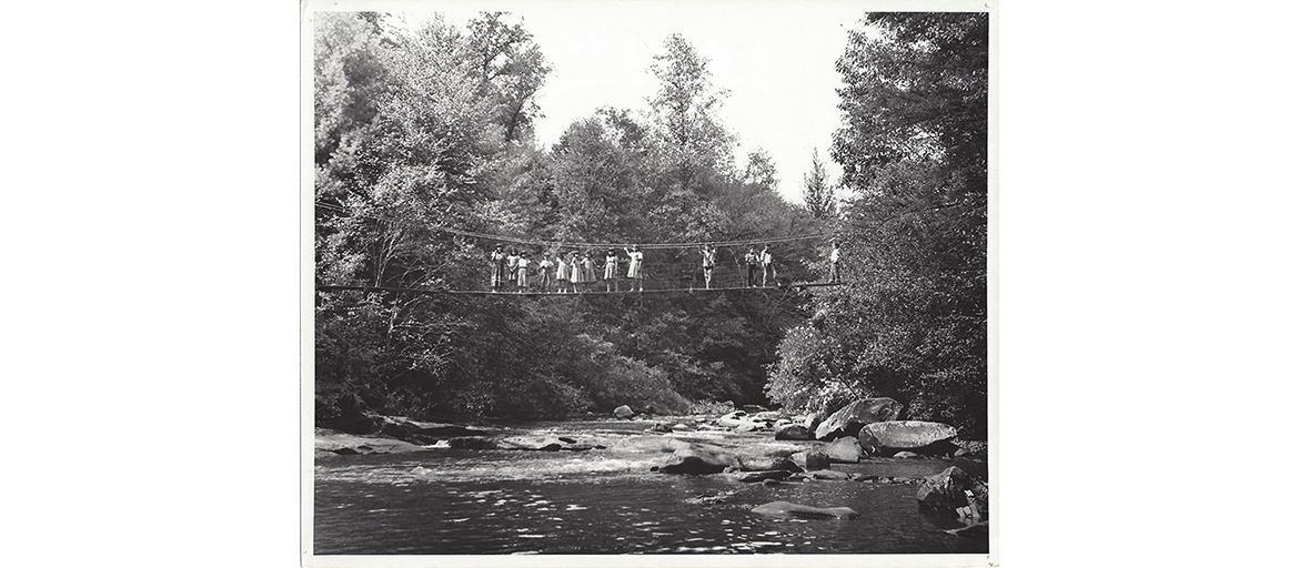 snowbird school – web old photo of children standing on a rope bridge above a mountain stream