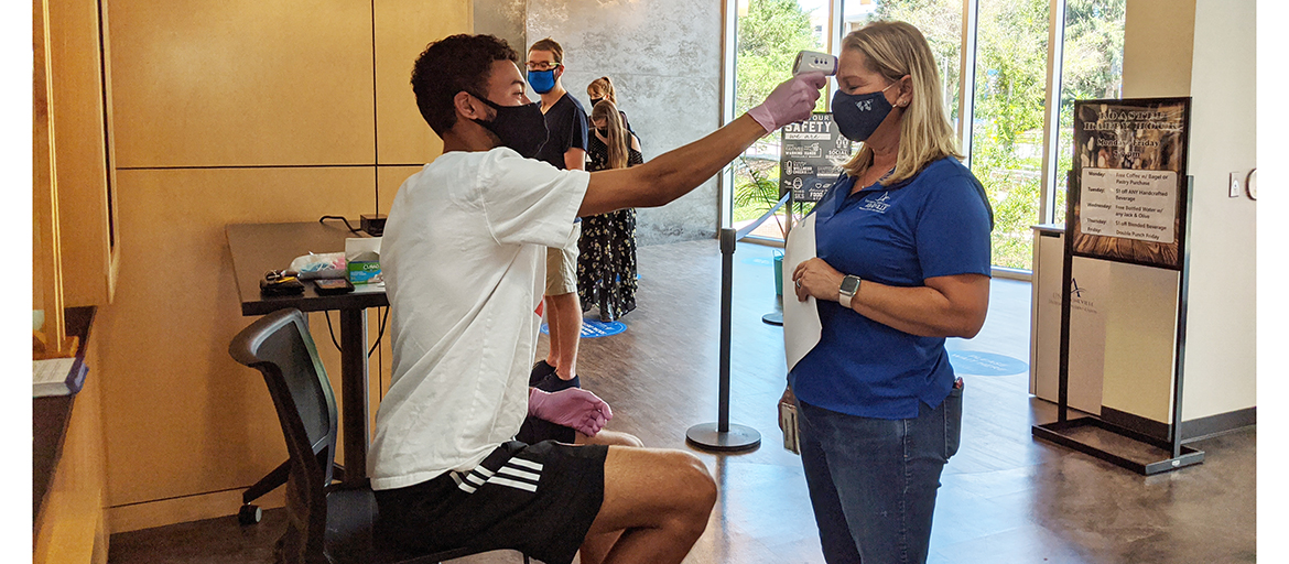 Student holds an infrared thermometer near the forehead of a university staff member