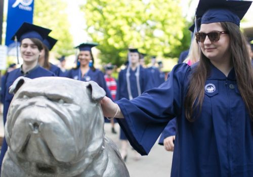 Students in caps and gowns walk past the bulldog mascot