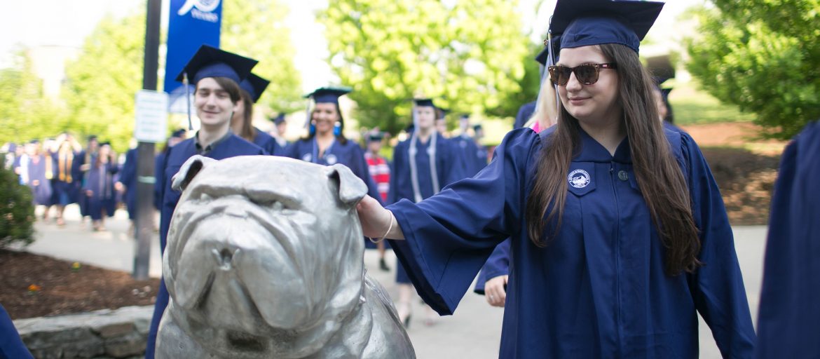 2018Commencement109-1170×512 Students in caps and gowns walk past the bulldog mascot