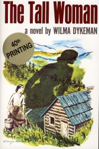 Book cover of "The Tall Woman" show a woman casting a shadow larger than a house