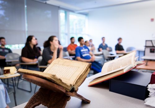 A close-up of two books in front of a classroom full of students.