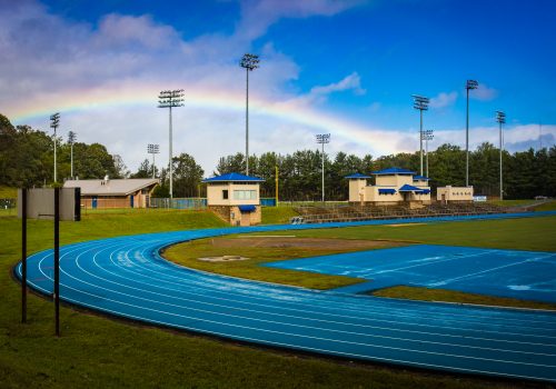 A track with bleachers and a rainbow behind it.