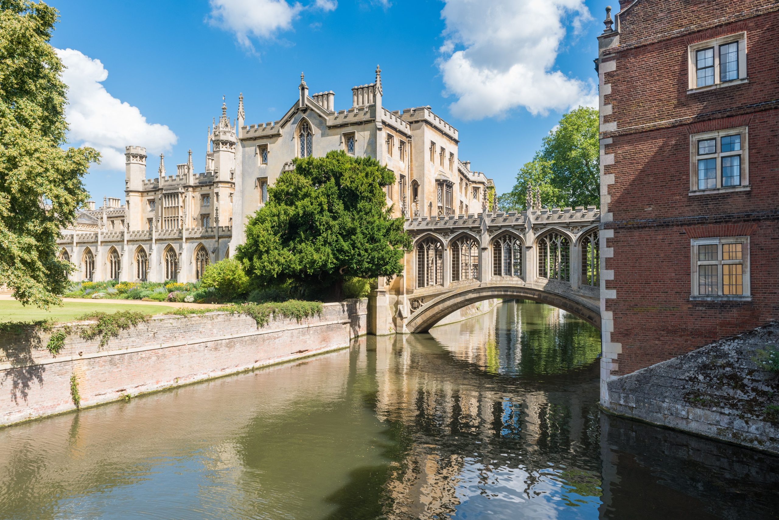 A stone bridge sitting over a canal with two buildings around the bridge.